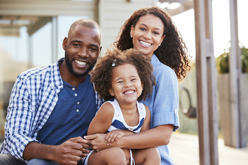 Image Text: Young black family embracing outdoors and smiling at camera